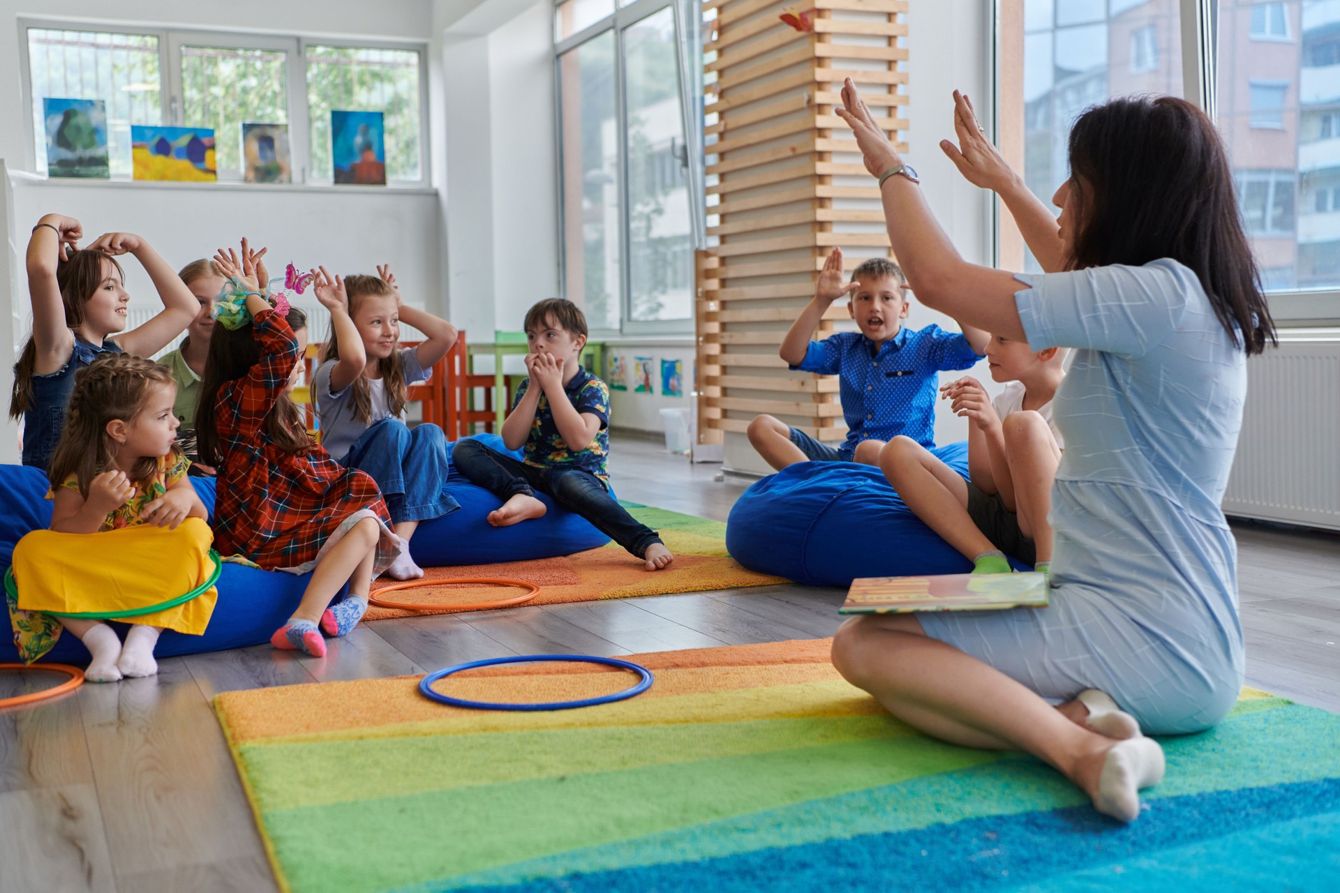 A happy female teacher sitting and playing hand games with a group of little schoolchildren