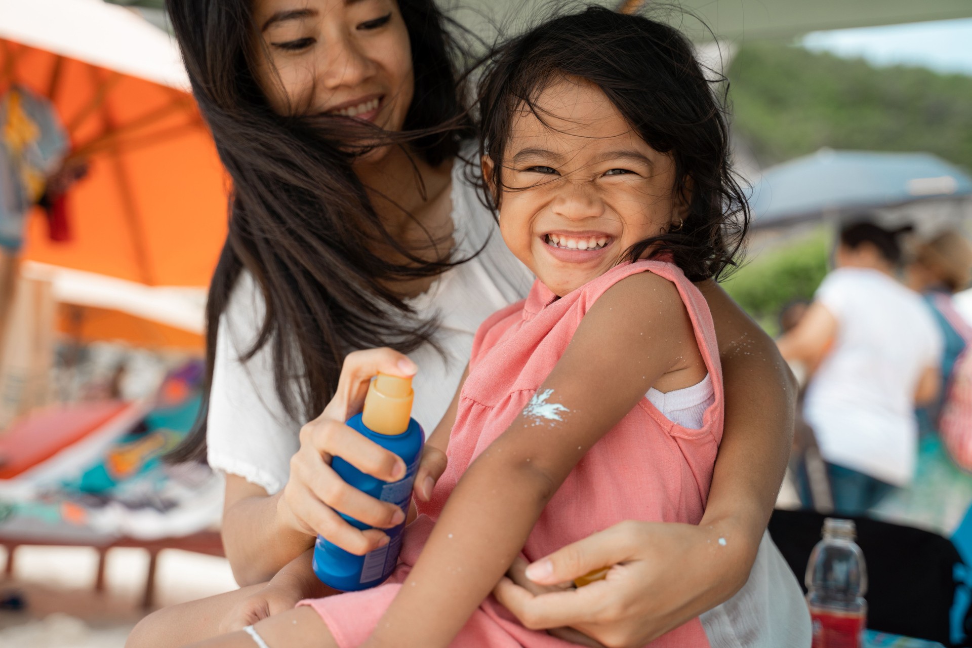 a happy daughter amused look at the camera when his mother give a sunblock